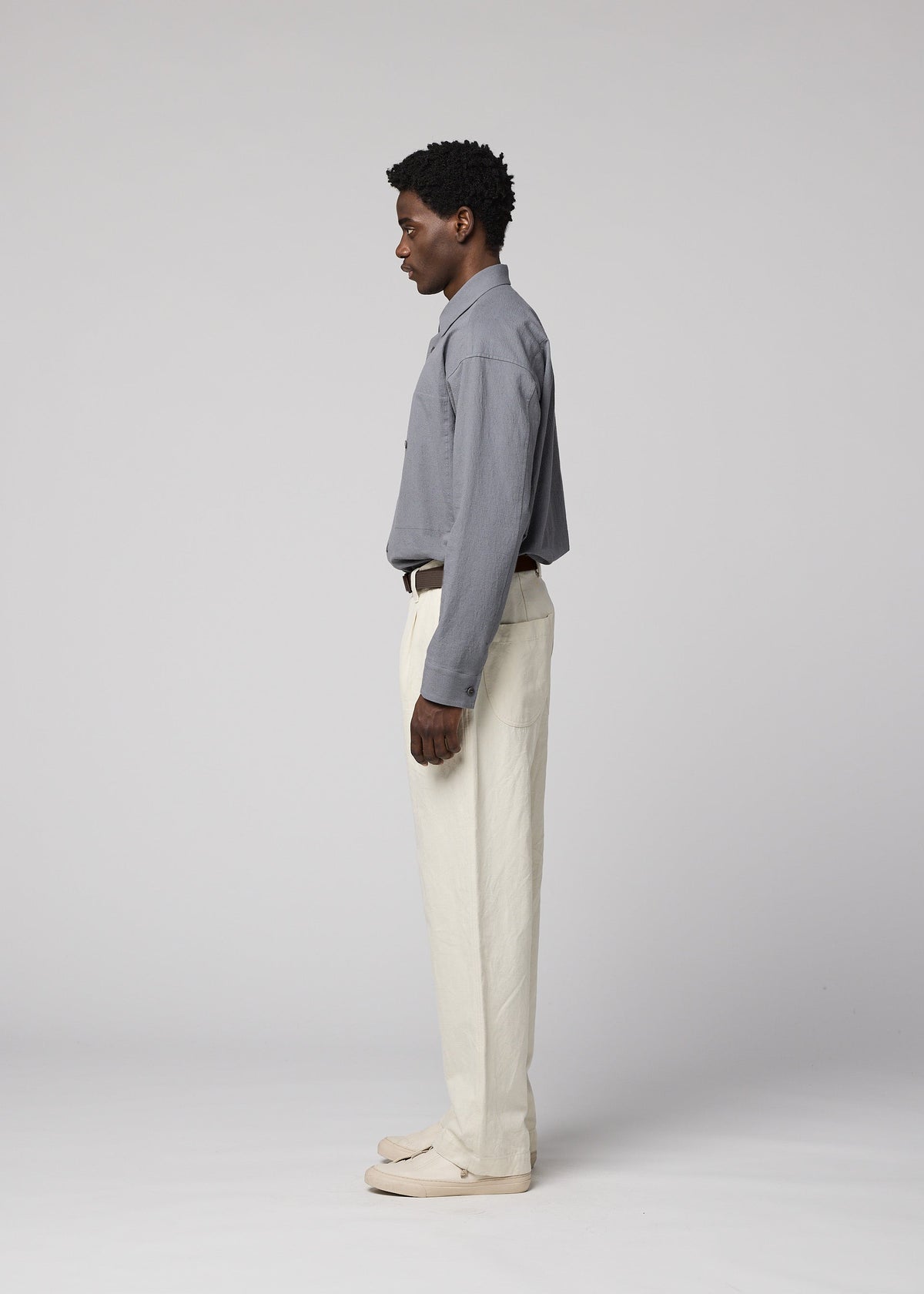 A man stands in profile against a plain light background, wearing a gray button-up shirt, IM MEN TOUGH WOOL COTTON pants in white, and light shoes. view 7 of 9