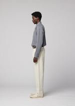 A man stands in profile against a plain light background, wearing a gray button-up shirt, IM MEN TOUGH WOOL COTTON pants in white, and light shoes.