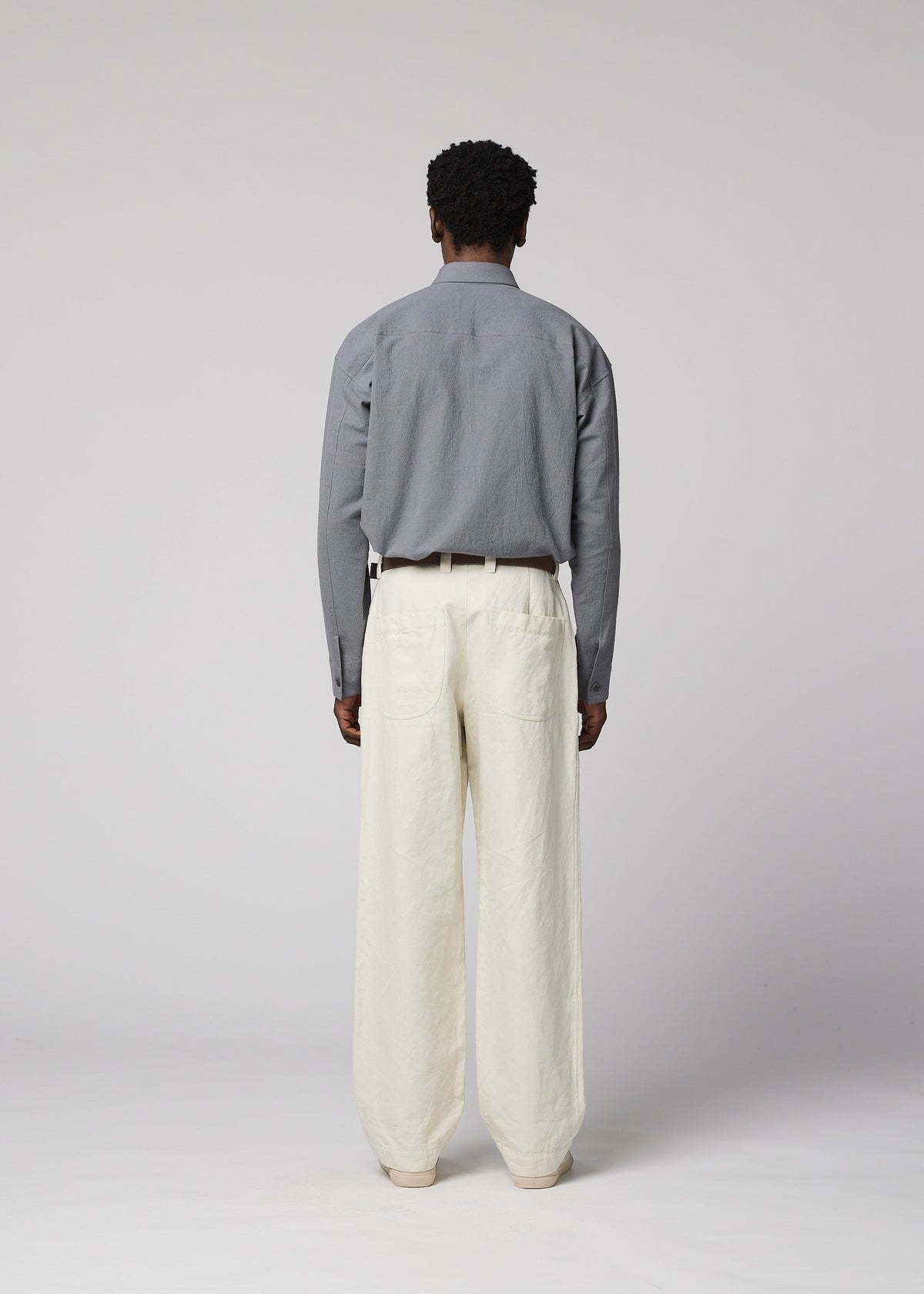 A person stands facing away, dressed in a gray long-sleeve shirt tucked into IM MEN’s TOUGH WOOL COTTON high-waisted pants with a black belt, set against a plain light gray background. view 8 of 9