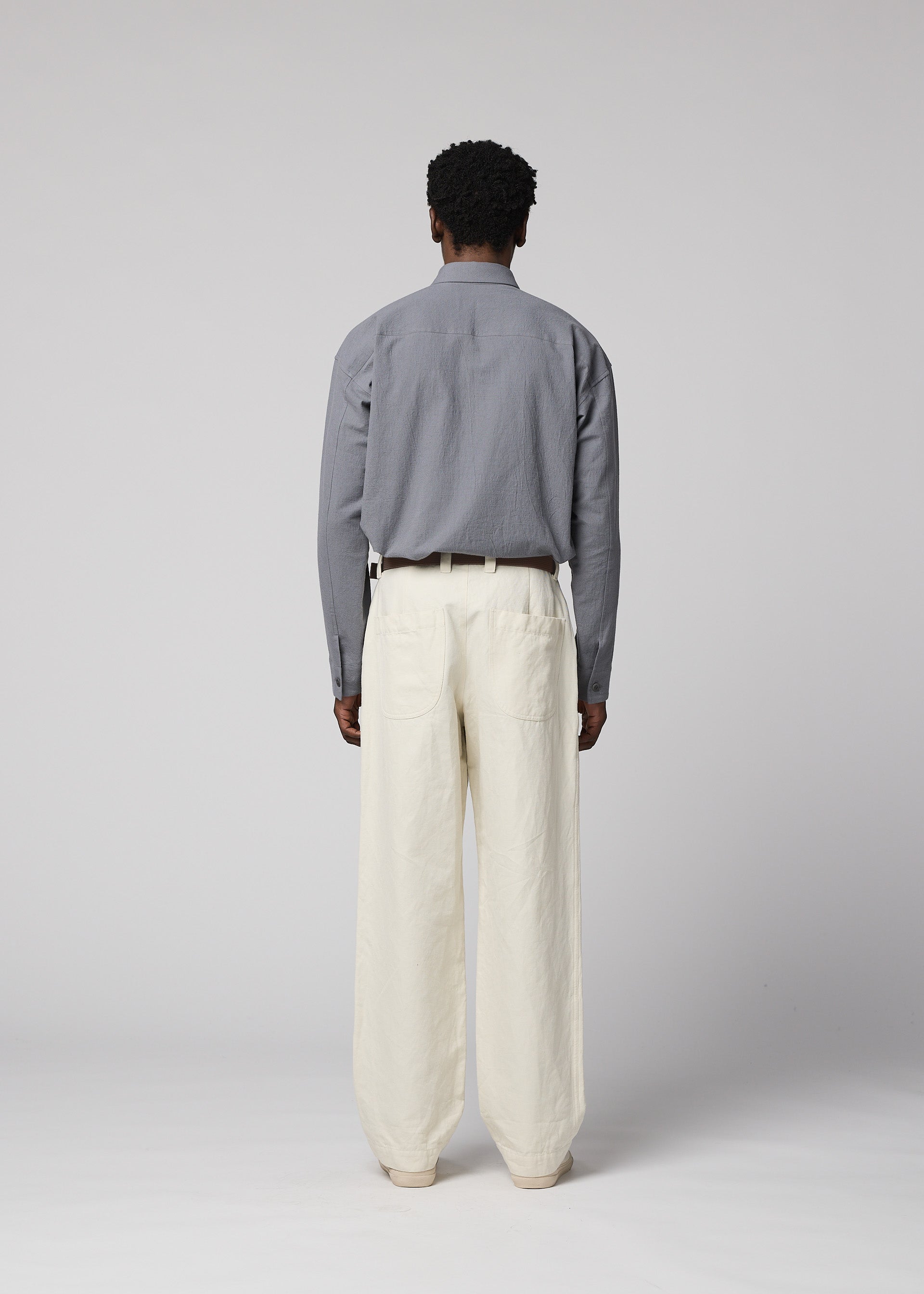 Zoomed view A person stands facing away, dressed in a gray long-sleeve shirt tucked into IM MEN’s TOUGH WOOL COTTON high-waisted pants with a black belt, set against a plain light gray background.