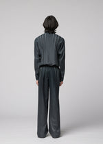 A person with medium-length dark hair stands facing away, wearing the IM MEN DAWN RAY dark, loose-fitting suit featuring vertical pinstripe details and transfer-printed pleated pants, set against a plain light gray background.