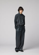 A person with medium-length dark hair stands against a plain light background, wearing the IM MEN DAWN RAY set—a loose-fitting, dark, shiny shirt paired with matching wide-legged pleated pants featuring stripe details—hands in pockets and styled with black shoes.
