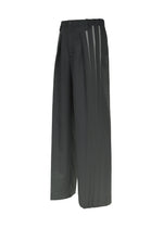 The IM MEN “DAWN RAY” trousers feature a wide-leg silhouette, transfer-printed black fabric with gray vertical stripe accents along the sides, a pleated front, and an elastic waistband, shown against a white background.