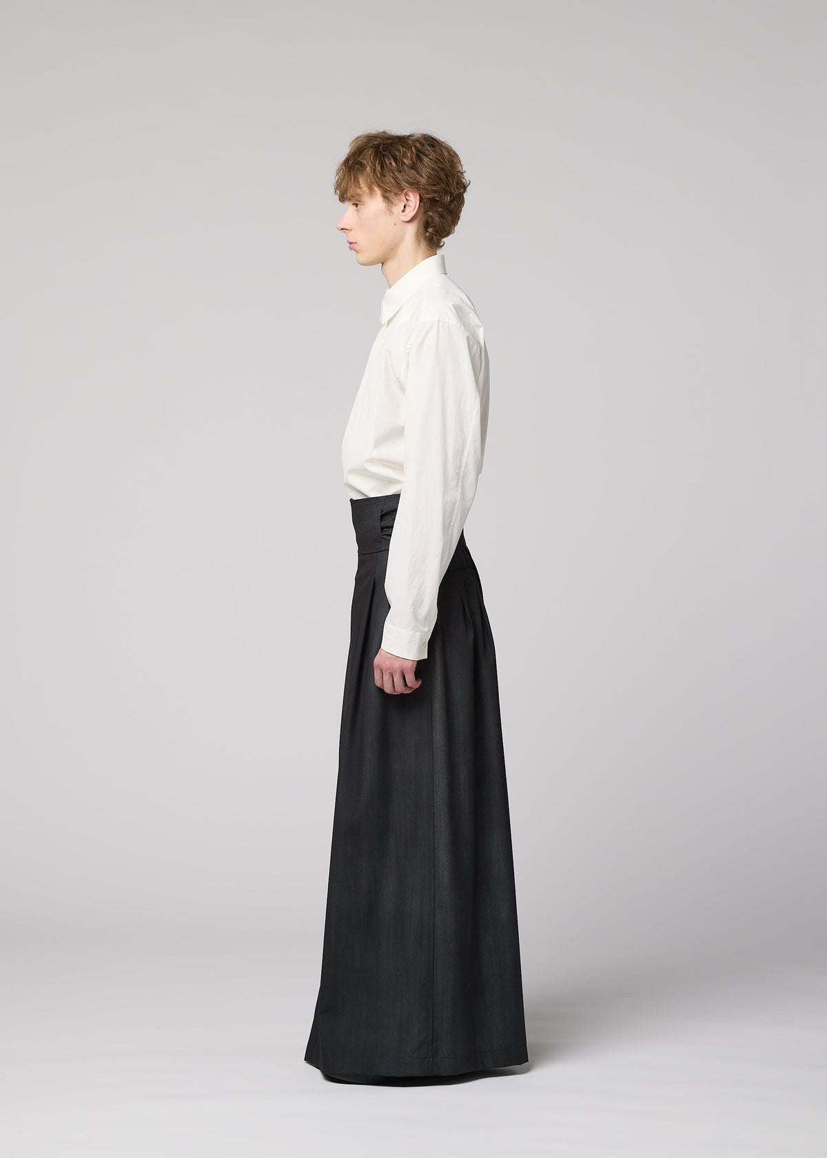 A person in profile wears a white long-sleeve shirt tucked into high-waisted GRADATION WOOL pants from IM MEN, standing against a plain light gray background. view 5 of 7
