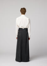 Person standing with back to camera, wearing a white long-sleeve shirt tucked into IM MEN GRADATION WOOL high-waisted, wide-leg pants against a plain light gray background.