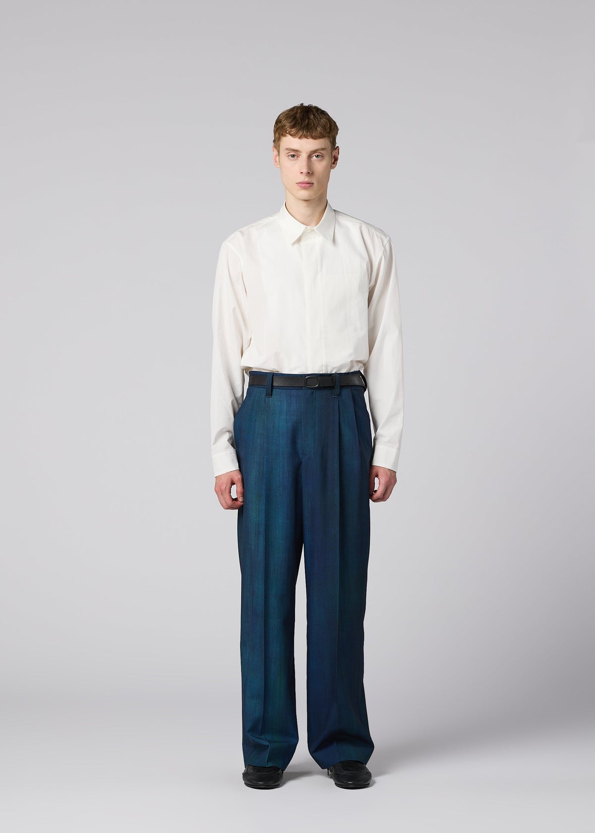 Zoomed view A person with short hair faces forward, wearing a white long-sleeve shirt tucked into high-waisted, loose GRADATION WOOL pants from IM MEN. The background is plain light gray.