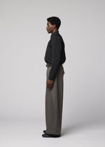 A man models IM MEN's OVERLAP collection, wearing a black button-up shirt and wide cotton-nylon blend pants, standing in profile against a plain light gray background with relaxed arms at his sides.