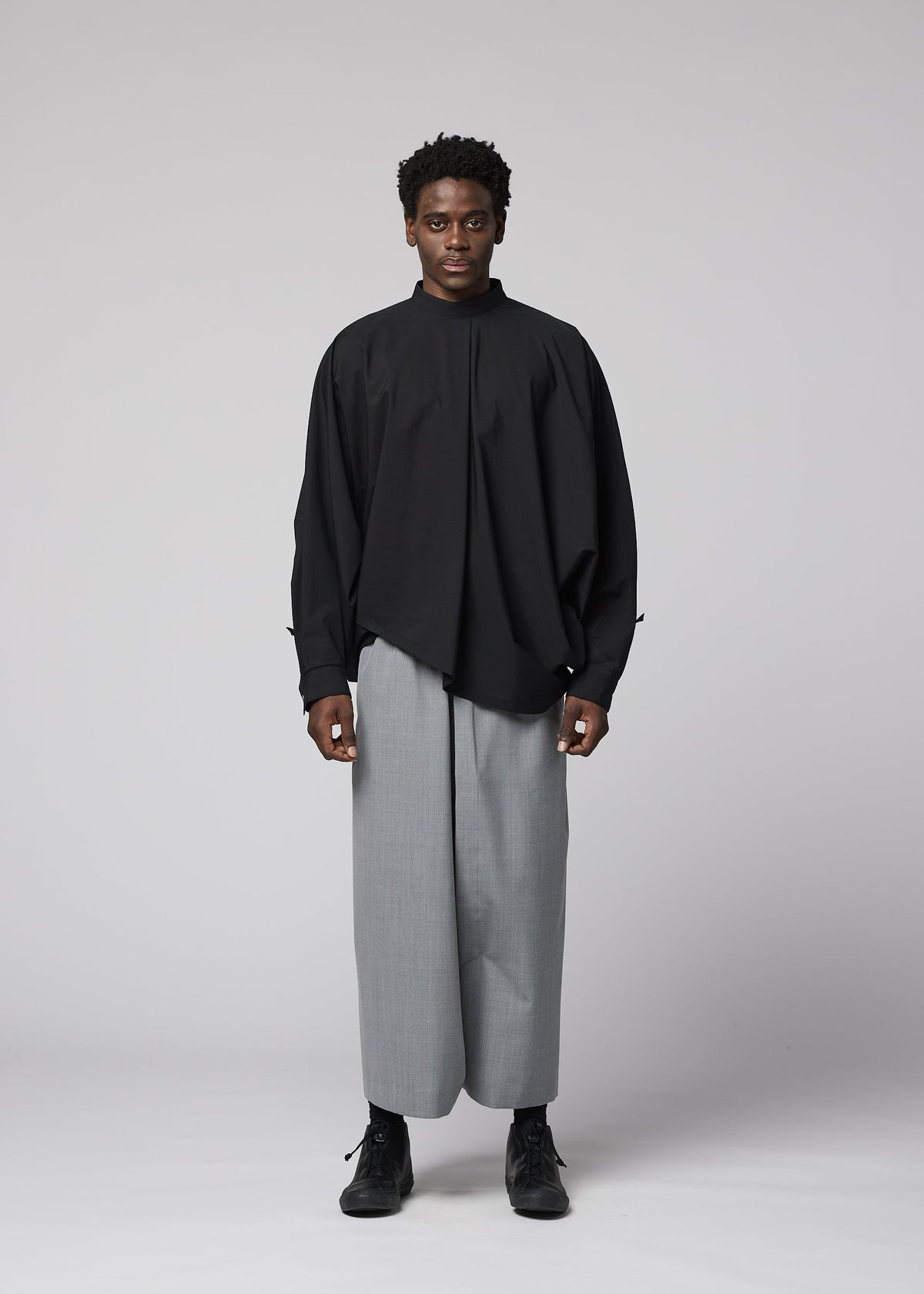 A person faces forward against a plain light background, wearing IM MEN’s SUAVE loose, long-sleeved black shirt and wide-legged wool blend sarouel pants with black shoes for a relaxed silhouette. view 6 of 9