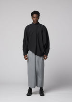 A person faces forward against a plain light background, wearing IM MEN’s SUAVE loose, long-sleeved black shirt and wide-legged wool blend sarouel pants with black shoes for a relaxed silhouette.