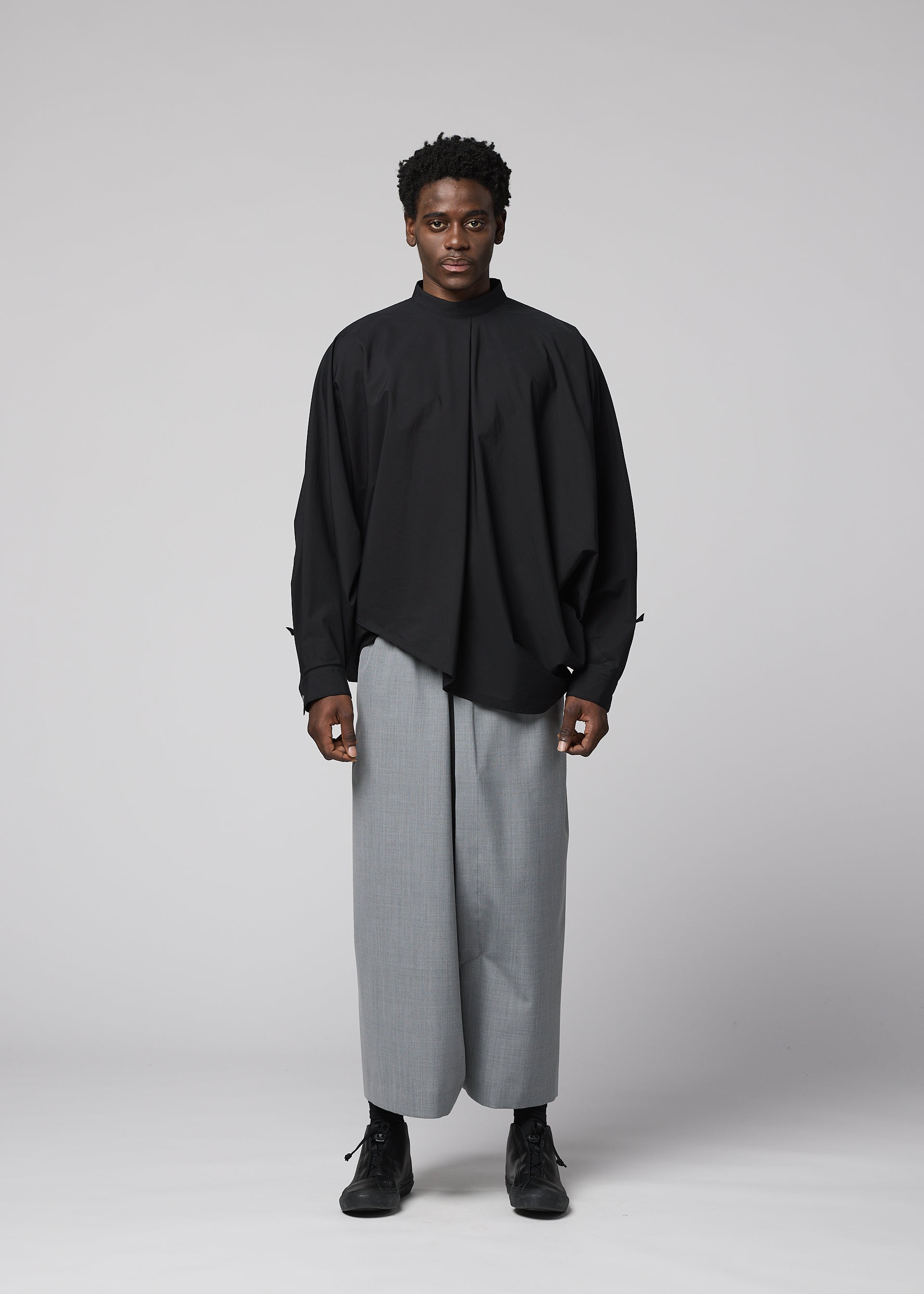 Zoomed view A person faces forward against a plain light background, wearing IM MEN’s SUAVE loose, long-sleeved black shirt and wide-legged wool blend sarouel pants with black shoes for a relaxed silhouette.