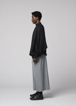 A person stands in profile against a plain backdrop, wearing IM MEN’s SUAVE loose black shirt and wide wool blend sarouel pants with black shoes—a minimalist, modern look with a relaxed silhouette.