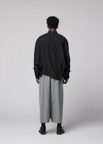 A person with short curly hair wears the IM MEN SUAVE loose black long-sleeve shirt with buttoned cuffs and wide wool blend sarouel pants, paired with black shoes, standing against a plain light gray background.