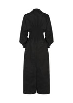 Back view of the CLAY dress by IM MEN, a long black piece crafted from rib knit fabric with long sleeves, a cinched waist, and a slightly flared skirt. Tailored for a flattering fit, it features gathered details at the upper back and draws inspiration from sculptural jumpsuit silhouettes showcased in the IM MEN Autumn Winter 2026/27 collection.