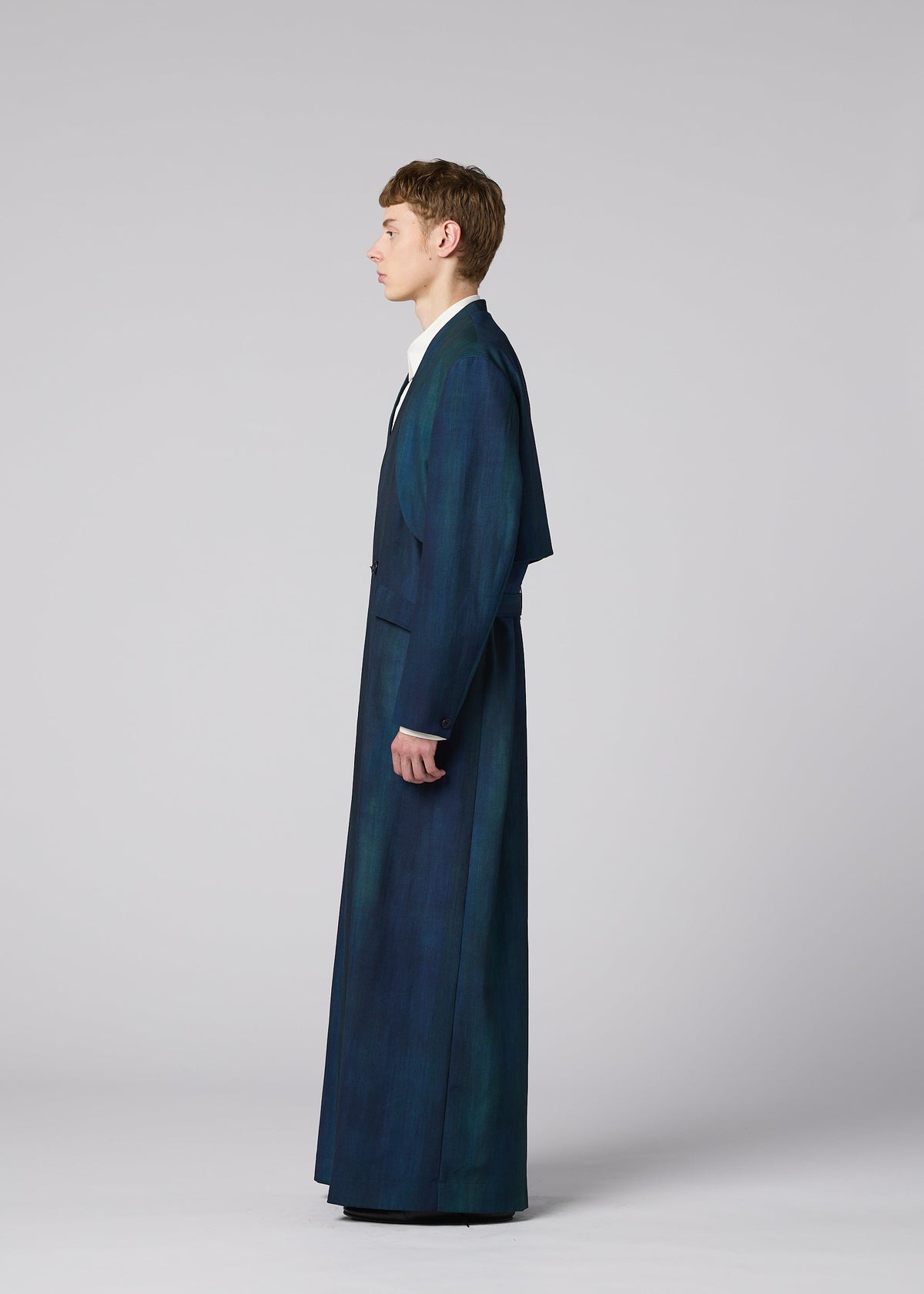 A person stands in profile against a plain background, wearing IM MEN’s GRADATION WOOL long dark blue tailored coat and matching wide-legged pants, with a white collared shirt underneath. view 10 of 13