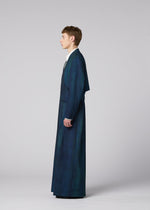 A person stands in profile against a plain background, wearing IM MEN’s GRADATION WOOL long dark blue tailored coat and matching wide-legged pants, with a white collared shirt underneath.