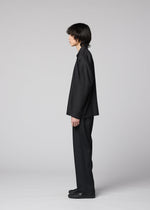 A person with medium-length dark hair stands in profile against a light gray background, wearing the IM MEN COMPACT SHIRT BLACK, complemented by matching black pants and black shoes.