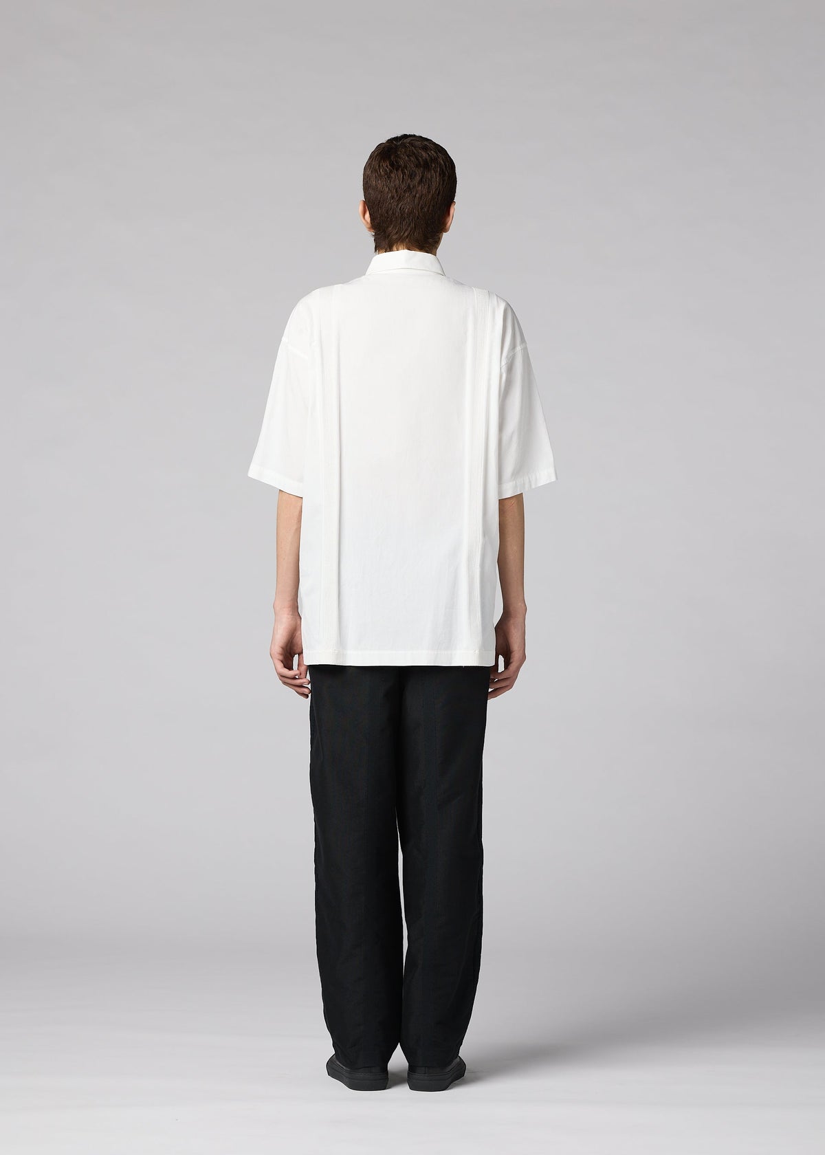 A person faces away from the camera in a loose white CLAY SHIRT by IM MEN and black pants, set against a light gray background. view 7 of 8