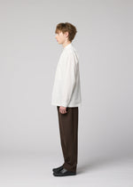 A person with light brown hair stands in profile against a plain gray background, wearing the IM MEN 140/2 SHIRT, loose brown pants, and black shoes.