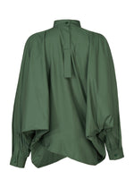 A back view of the IM MEN 140/2 SHIRT shows its loose fit, dark green band collar, long wide sleeves, tab detail at the upper back, and a relaxed silhouette with a unique draped, overlapped hem.