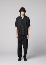 A person with medium-length dark hair faces forward, wearing the IM MEN COMPACT SHIRT in black, made of light wrinkle-resistant material, along with matching black pants and shoes, against a plain light gray background.