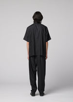 A person with straight, dark hair faces away from the camera, wearing the IM MEN COMPACT SHIRT—a wrinkle-resistant, lightweight black short-sleeved shirt—paired with matching black pants, set against a plain gray background.