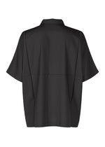 The IM MEN COMPACT SHIRT is a loose-fit, short-sleeved black shirt with a collar and straight hem, made from wrinkle-resistant lightweight material for comfortable wear. Shown here in a back view.