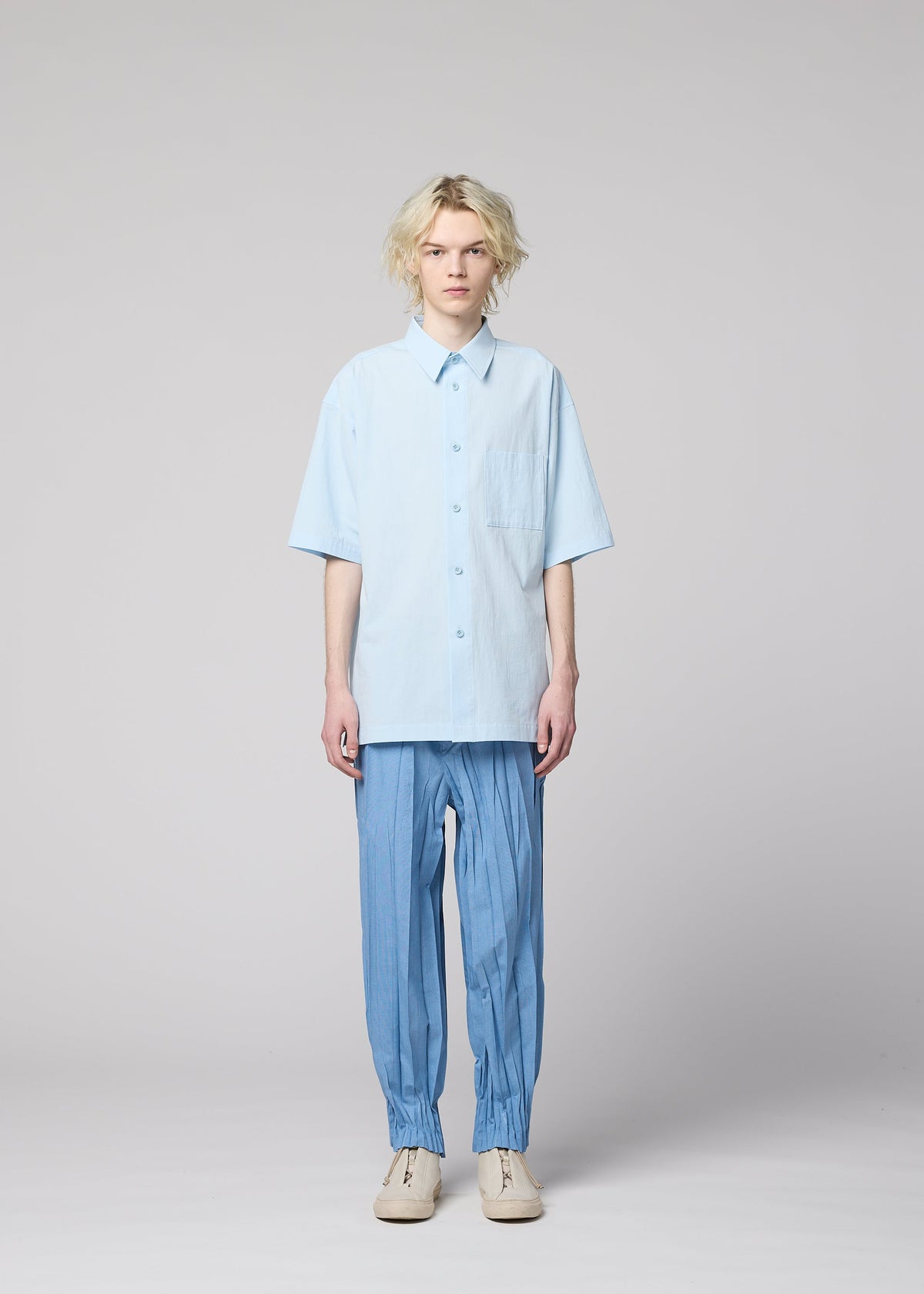 Person with wavy blond hair wears a light blue cotton linen ramie short-sleeved regular-collar shirt and loose blue pants with ankle cuffs, standing against a plain light background. view 6 of 9