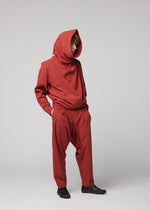 A person stands with hands in pockets, dressed in a loose-fitting red COTTON YAK hooded outfit from IM MEN, paired with baggy pants and black shoes, set against a plain light gray background—a look inspired by the IM MEN Autumn Winter 2026/27 collection.