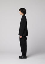 A person with medium-length dark hair stands in profile against a plain light gray background, wearing loose-fitting black pants, black shoes, and the IM MEN COTTON YAK long-sleeved shirt that highlights its natural texture.