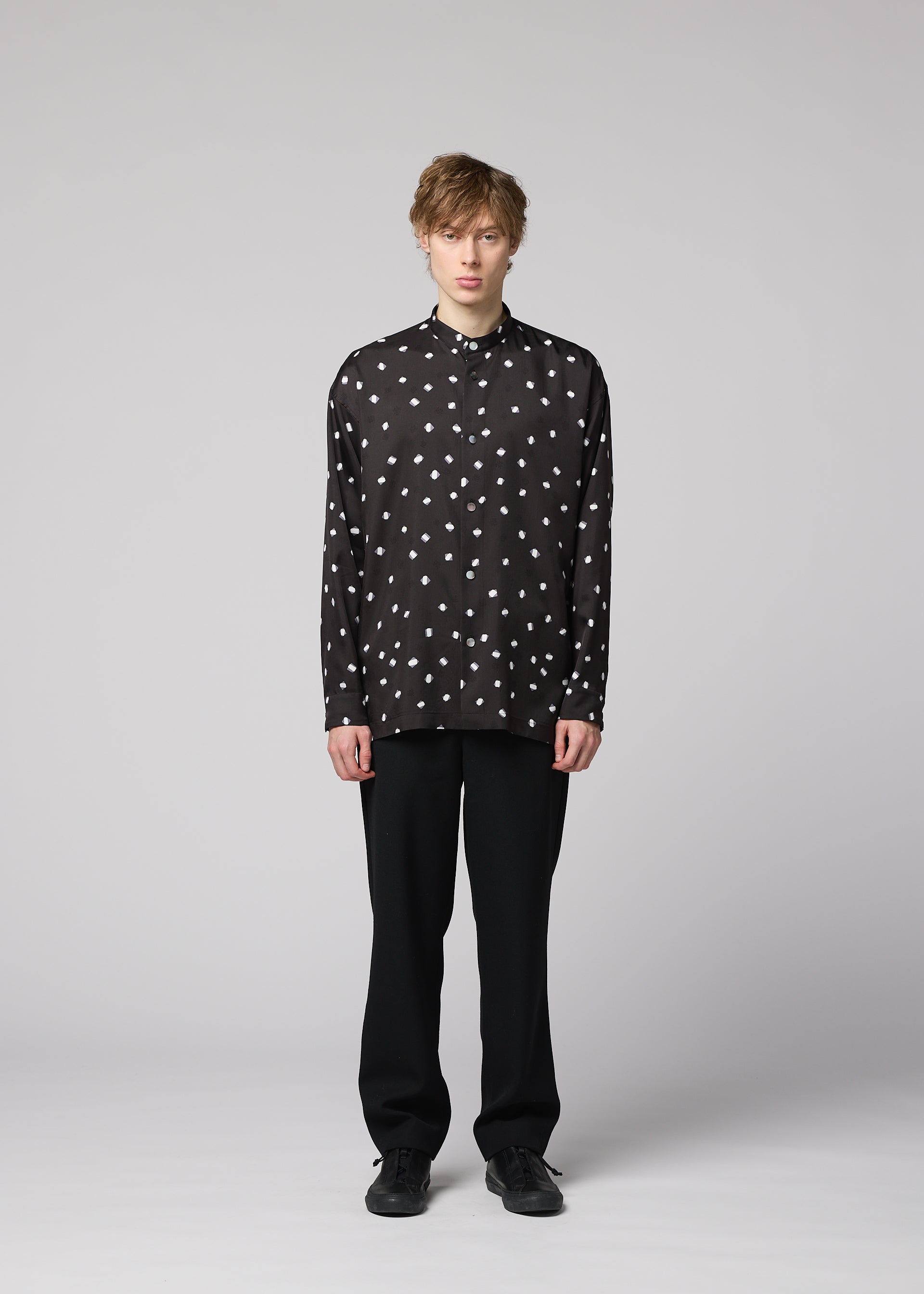Zoomed view A person with light brown hair stands facing forward, dressed in a black MERRY SATIN SHIRT by IM MEN with white polka dots, paired with black pants and black shoes, against a plain light grey background.