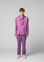 A person stands against a plain background, wearing the IM MEN MERRY SATIN SHIRT in purple with white polka dots, paired with matching purple pants and white shoes. Their expression is neutral and their posture relaxed.