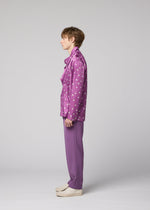 A person stands in profile against a gray background, wearing the MERRY SATIN SHIRT by IM MEN—a shiny satin shirt with white polka dots—paired with matching purple pants and off-white shoes.
