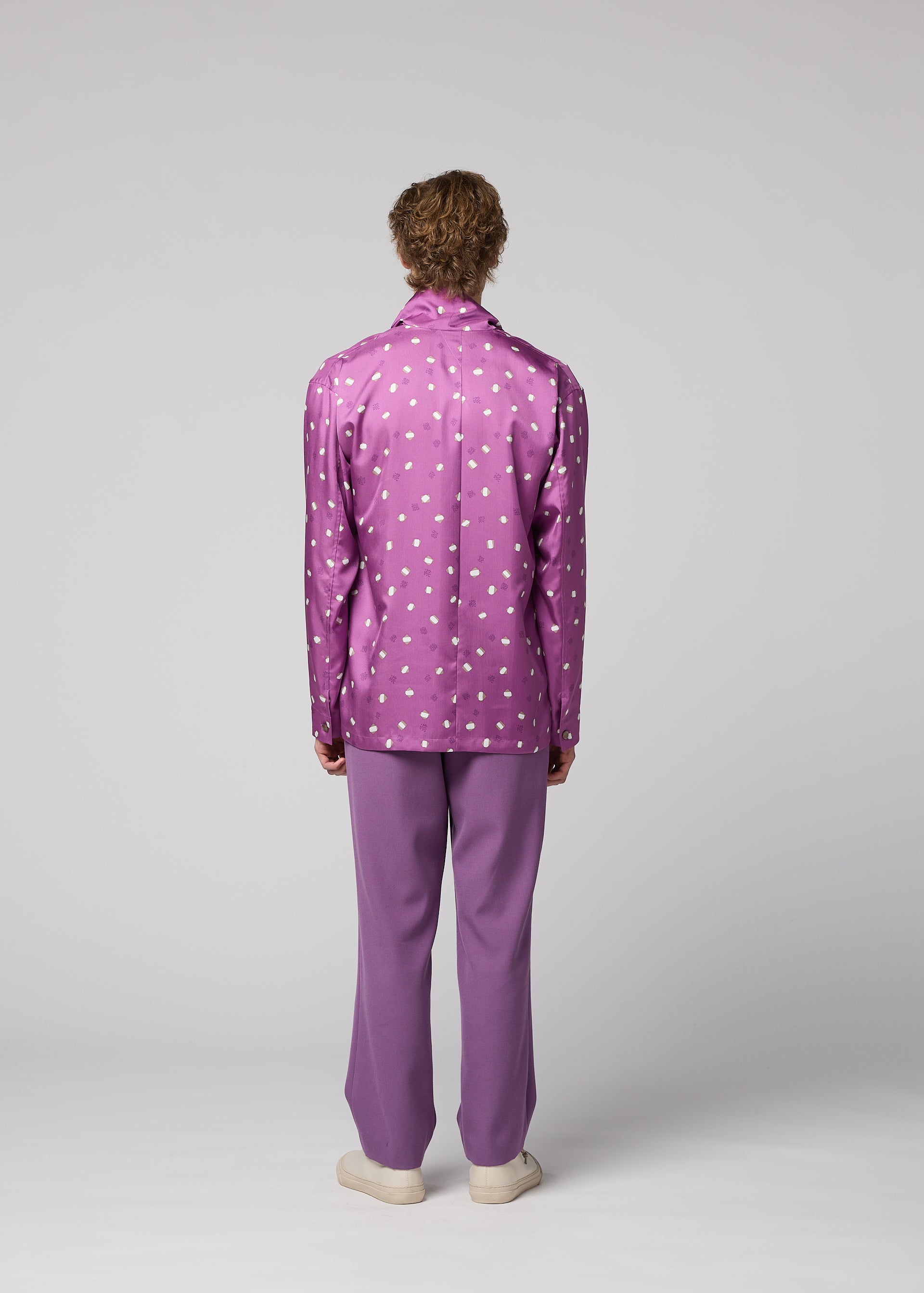 Zoomed view A person stands facing away, wearing the IM MEN MERRY SATIN SHIRT in purple with polka dots, paired with matching purple pants and white shoes, set against a plain gray background.