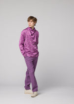 A person stands against a plain light gray background, wearing the IM MEN MERRY SATIN SHIRT in purple with polka dots, paired with matching purple pants and white shoes.