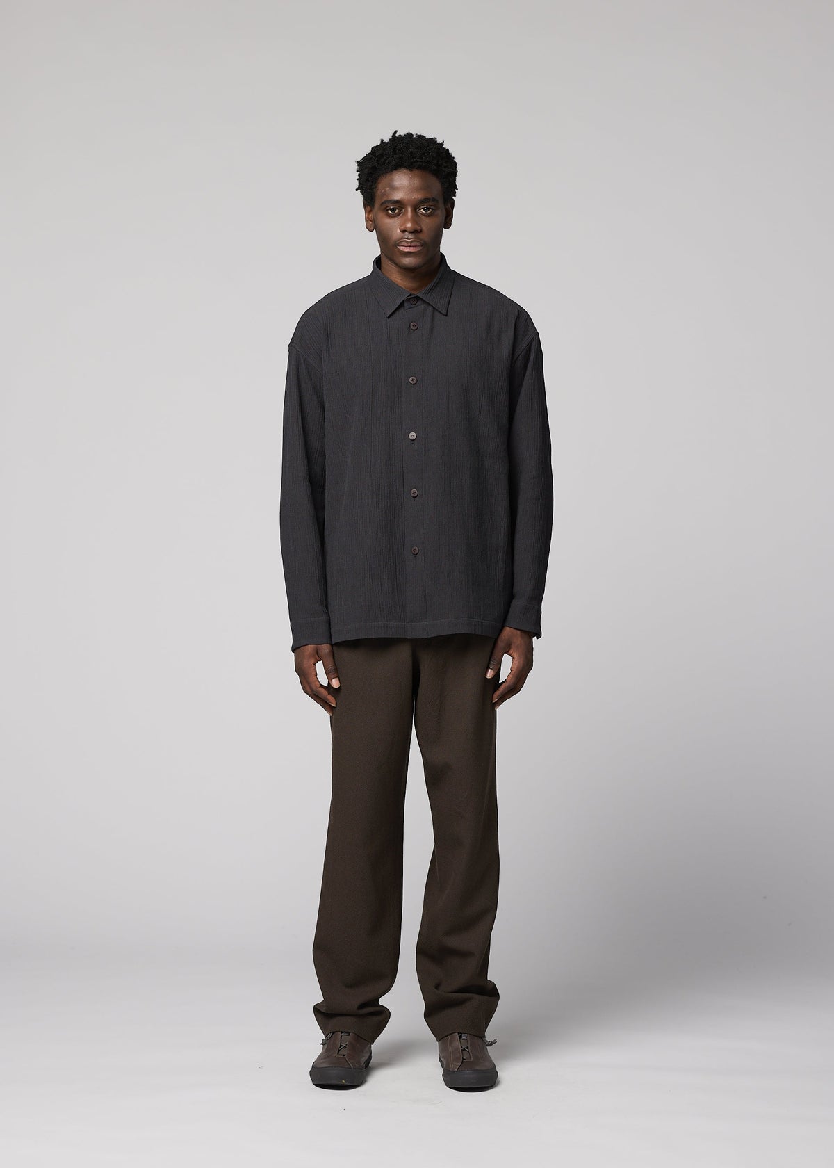A man faces the camera against a plain background, wearing the IM MEN DOUBLE WEAVE CREPE dark long-sleeved shirt, brown pants, and brown shoes with a neutral expression and relaxed arms. view 5 of 8