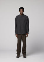 A man faces the camera against a plain background, wearing the IM MEN DOUBLE WEAVE CREPE dark long-sleeved shirt, brown pants, and brown shoes with a neutral expression and relaxed arms.
