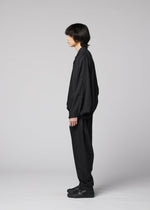 A person with medium-length dark hair stands in profile against a plain grey background, wearing the IM MEN SWING BLACK wrinkle-resistant, collarless jacket paired with matching black shoes.
