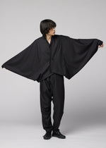 A person in loose, all-black clothing poses with arms extended, highlighting the wide, flowing SWING BLACK jacket by IM MEN, reminiscent of bat wings against a plain light background.