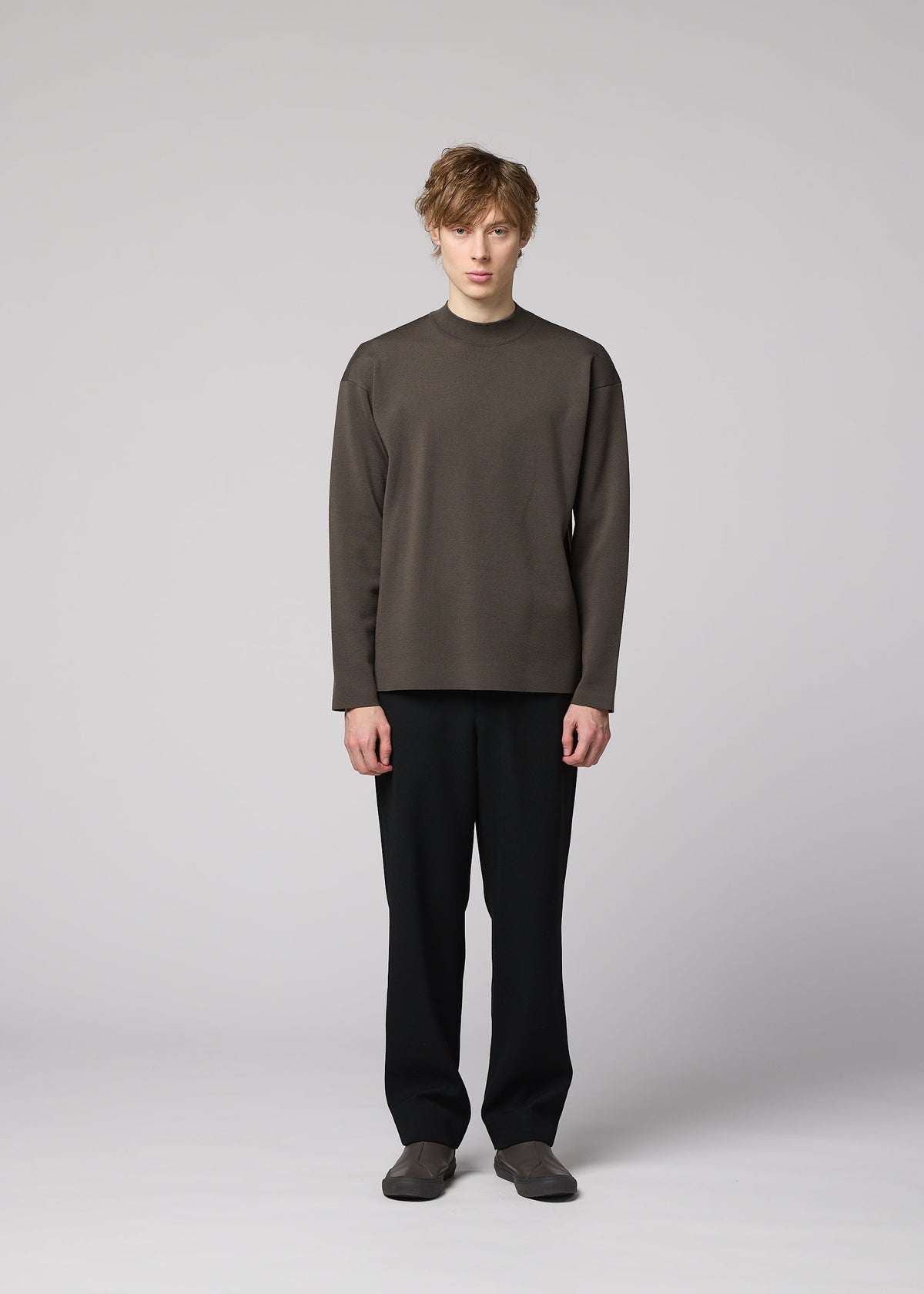 A person stands against a plain light gray background, wearing the IM MEN MONO-MILANO loose-fitting brown Milano ribbed pullover, made from wrinkle-resistant, washable wool, paired with black pants and brown shoes, facing forward with a neutral expression. view 4 of 6