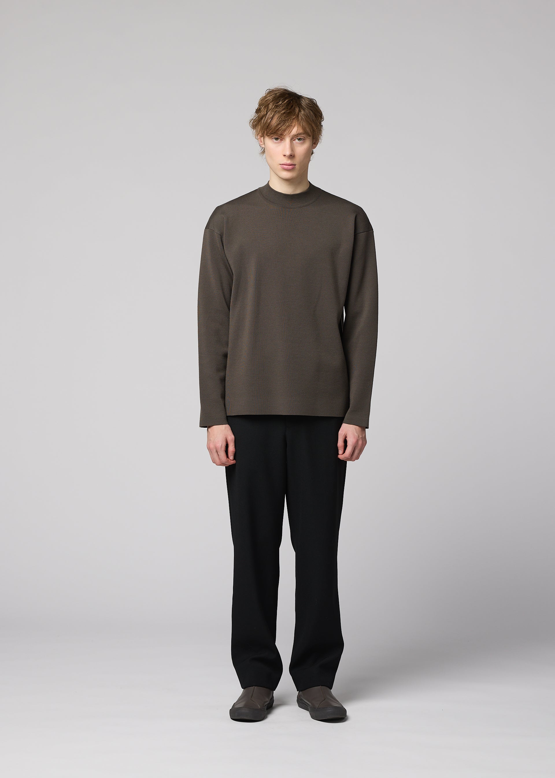 Zoomed view A person stands against a plain light gray background, wearing the IM MEN MONO-MILANO loose-fitting brown Milano ribbed pullover, made from wrinkle-resistant, washable wool, paired with black pants and brown shoes, facing forward with a neutral expression.
