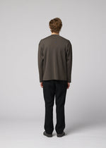 A person stands facing away from the camera, wearing IM MEN’s MONO-MILANO loose dark gray pullover and black pants against a plain light gray background. The wrinkle-resistant fabric of the MONO-MILANO ensures a polished look all day long.