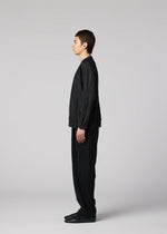 A person with short brown hair stands in profile against a light gray background, wearing IM MEN’s RIPPLE KNIT: a dynamic black long-sleeve top paired with loose black pants and black shoes.