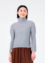 A woman with straight dark hair, dressed in the me ISSEY MIYAKE STRETCH PLEATS 7 light gray pleated long-sleeve top and brown pleated pants, stands against a white background and smiles slightly while looking to her left.