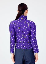 A person with long dark hair in a low ponytail is seen from the back wearing me ISSEY MIYAKE's TIME DOTS high-neck top featuring an abstract black, white, and yellow-green dotted pattern, paired with dark blue pants.