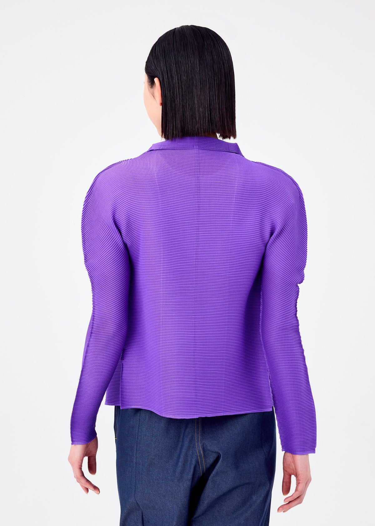 A person with straight, shoulder-length dark hair is shown from the back, wearing a vibrant purple me ISSEY MIYAKE STRETCH PLEATS 7 long-sleeved cardigan with structured shoulders and dark blue pants against a white background. view 6 of 7