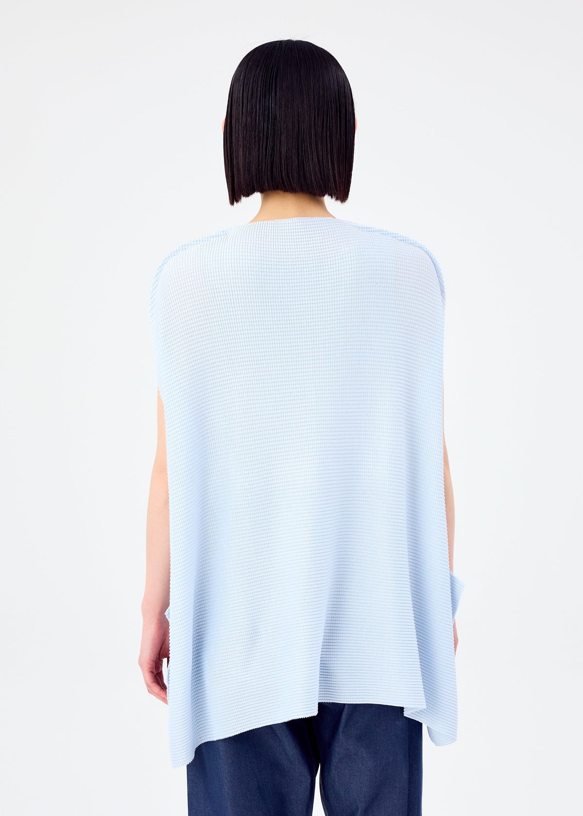 A person with straight, chin-length dark hair stands with their back to the camera, wearing the CURVE KNIT STRETCH PLEATS top by me ISSEY MIYAKE in light blue and dark blue pants against a plain white background. view 7 of 8