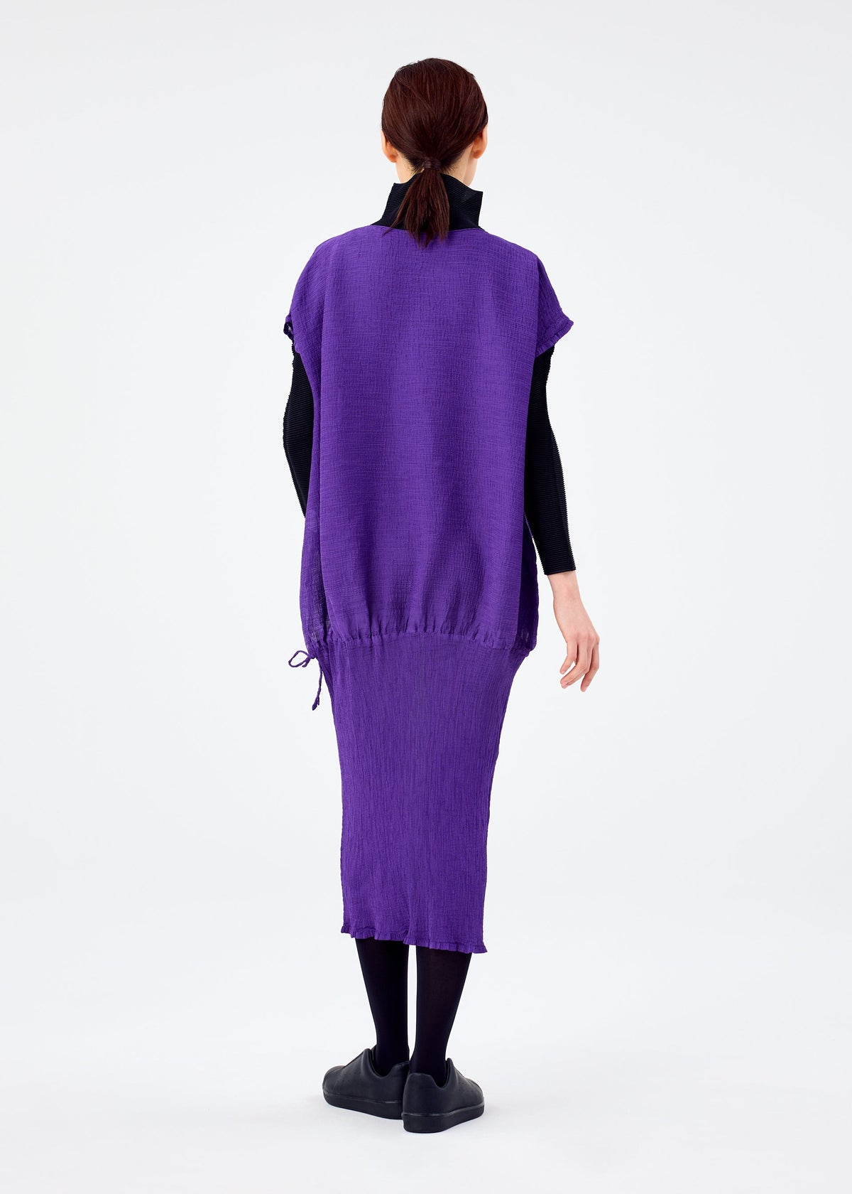 A person with brown hair tied back faces away, wearing the me ISSEY MIYAKE BALLOON SEE-THROUGH CREPE dress over a black turtleneck, black tights, and black shoes against a plain white background. view 6 of 6