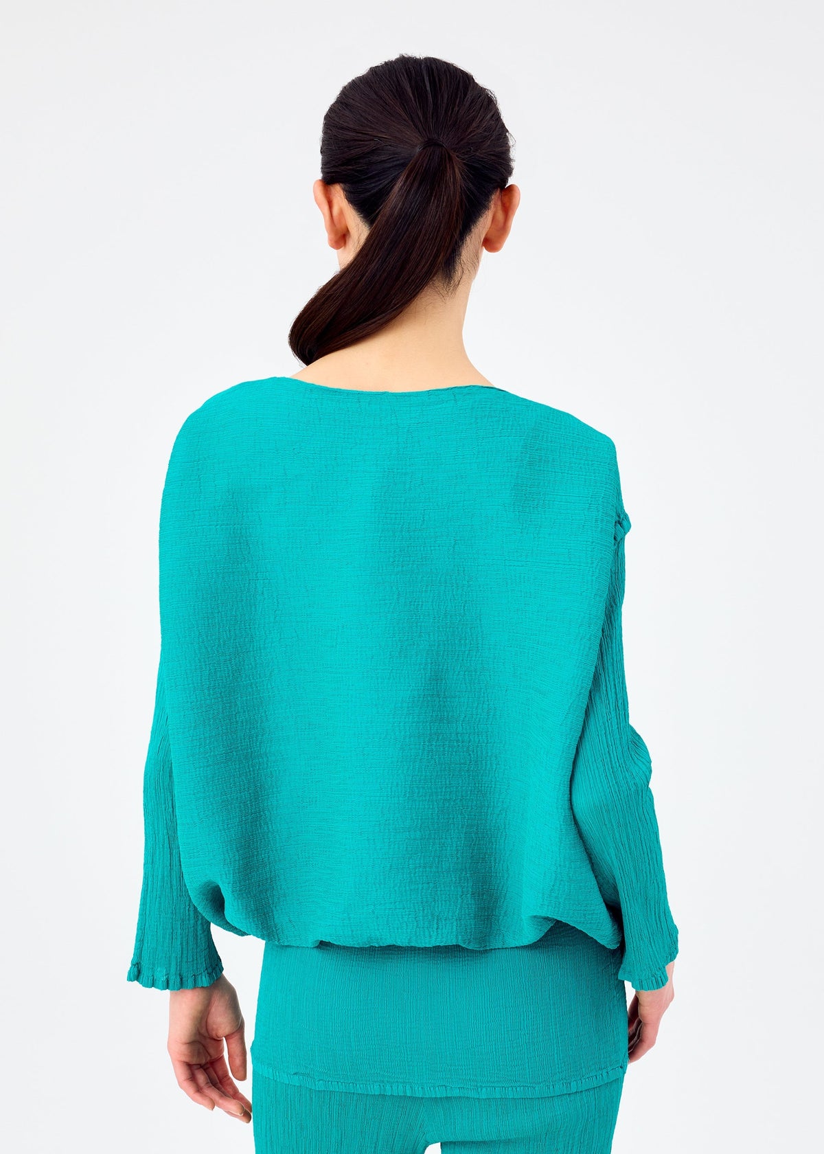 A woman with dark hair tied back is shown from behind, wearing the me ISSEY MIYAKE BALLOON SEE-THROUGH CREPE set in turquoise against a plain light background. view 6 of 7