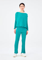 A woman faces forward in a loose, crinkled-texture turquoise BALLOON SEE-THROUGH CREPE blouse and matching pants by me ISSEY MIYAKE, paired with white shoes against a plain white background.