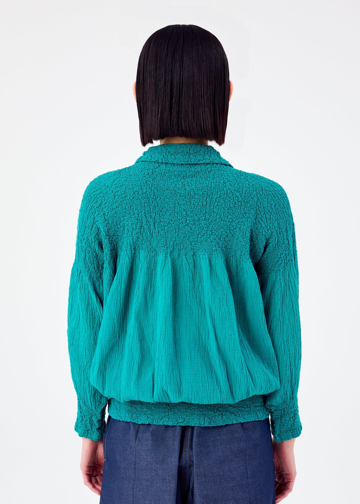 A person with straight, shoulder-length dark hair is seen from behind wearing the BALLOON CAULIFLOWER cardigan by me ISSEY MIYAKE in teal, paired with dark blue pants against a plain white background. view 6 of 7